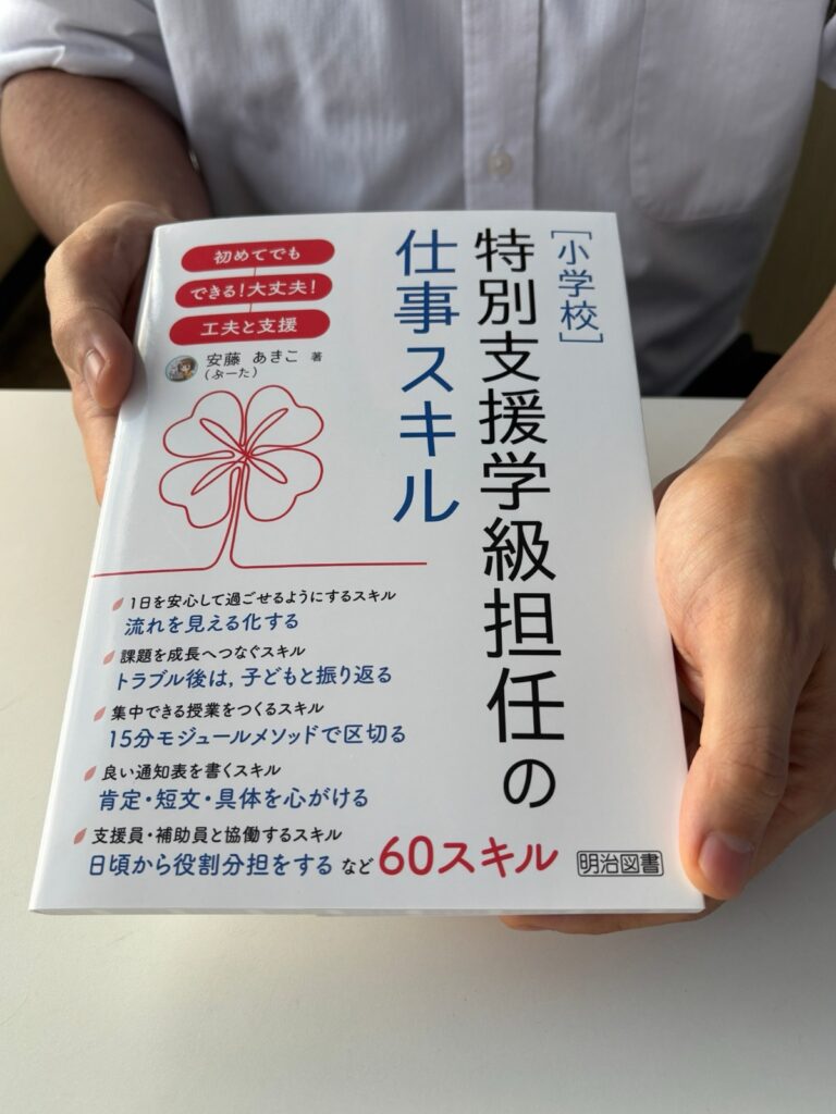 『［小学校］特別支援学級担任の仕事スキル』の表紙を、両手で持って見せている手元